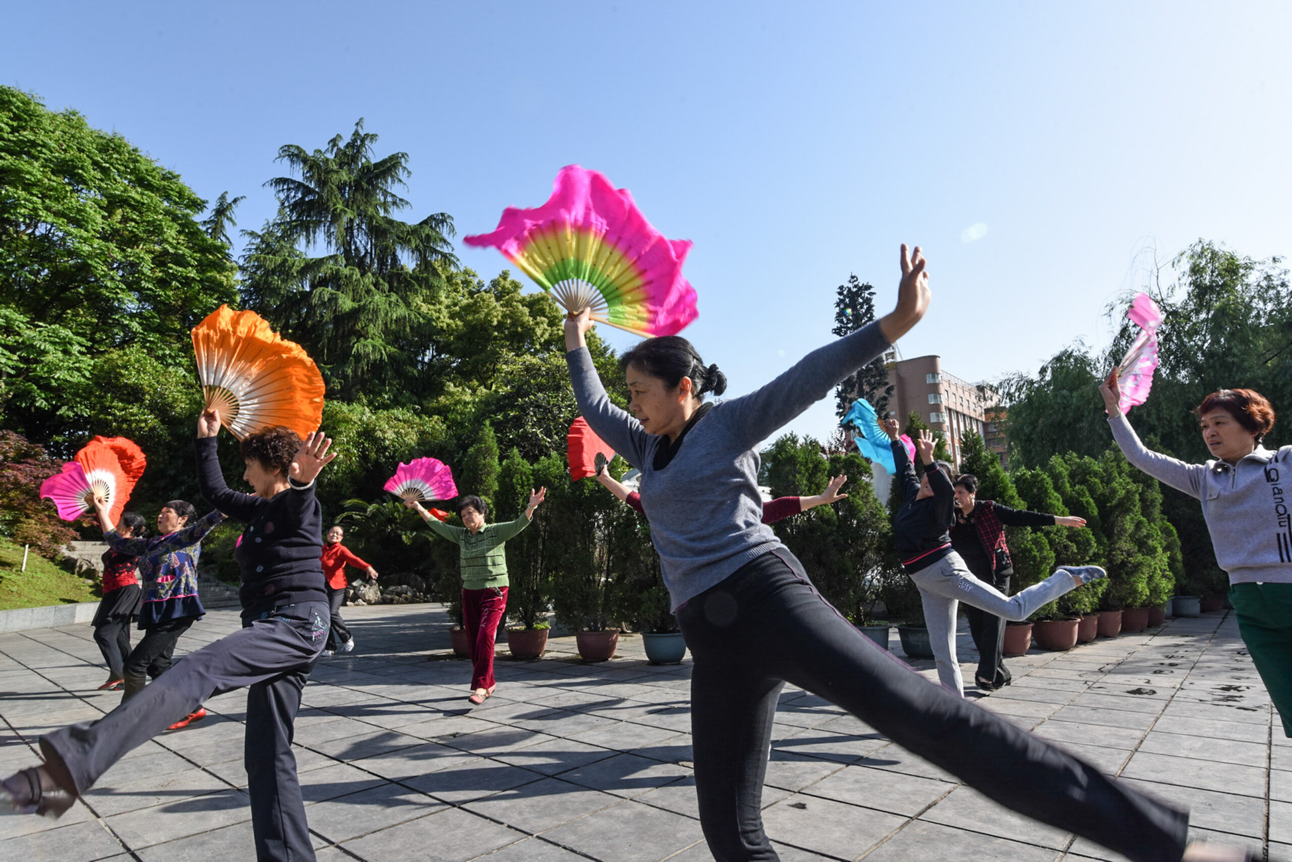 Citizens are doing morning exercises in a street garden.
